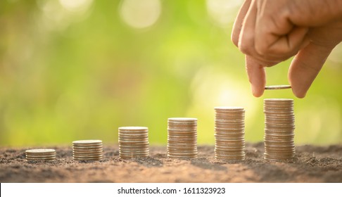 Close up hand putting coins in stack on wooden plank with green blur background. Money, Finance or Savings concept