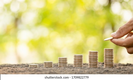 Close up hand putting coins in stack on wooden plank with green blur background. Money, Finance or Savings concept