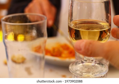 Close Up Of Hand Raising Glass With White Wine For A Toast, Photo Taken At Outdoor Restaurant In Front Of A Plate Of Pasta, Focus On The Glass, Background Out Of Focus.