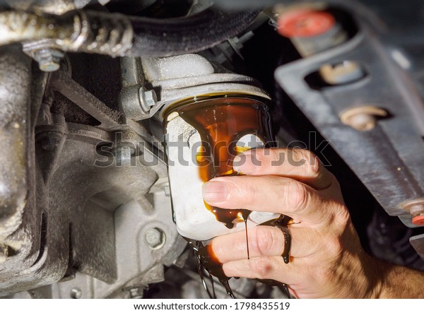 Close up of  a hand removing an oil filter\
on the underside of a car with oil\
dripping