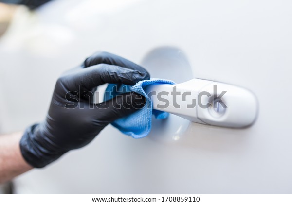 Close up of hand in rubber\
glove wiping car door handle. Virus and bacteria prevention\
concept.