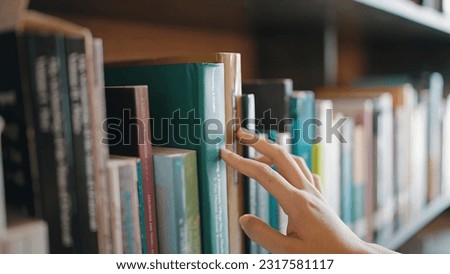 Close up hand search for book on bookshelves in the library. Select a book on shelf. Studying knowledge education in bookstore