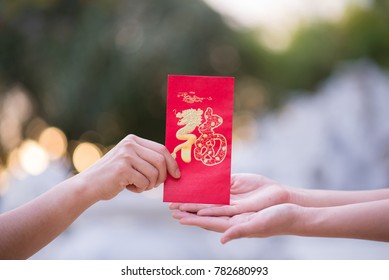 Close Up Hand Sending And Receiving Red Envelope Symbols Of The Chinese New Year On Golden Bokeh Background. Gifts, Festivals And Celebration Concept