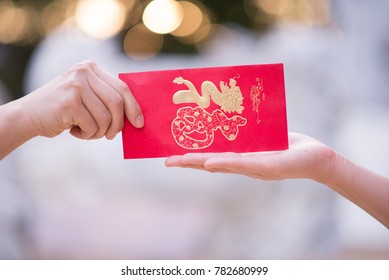 Close Up Hand Sending And Receiving Red Envelope Symbols Of The Chinese New Year On Golden Bokeh Background. Gifts, Festivals And Celebration Concept