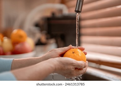 Close up hand of senior woman housewife wash orange in kitchen at home. Attractive mature housekeeper cleaning and rinse healthy fruits and vegetables with clean water to prepare breakfast in house. - Powered by Shutterstock