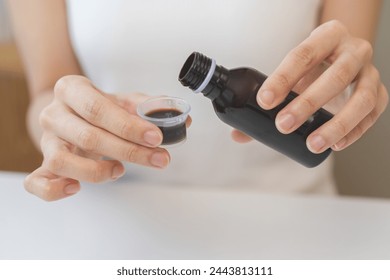 Close up hand of sick woman pouring syrup, liquid antipyretic, cough, flu medicine to jar from bottle, measuring dosage of drug with cup, taking therapy, treatment cure of disease. Health care concept - Powered by Shutterstock