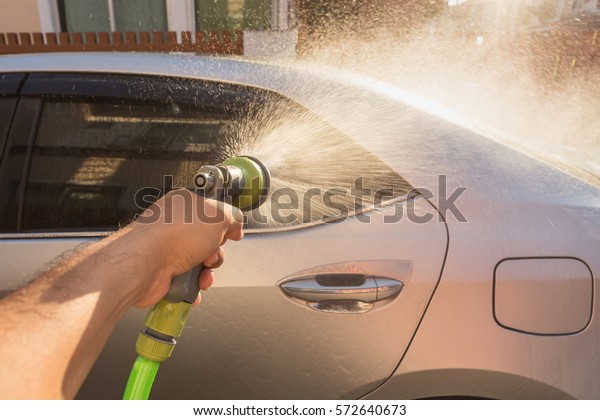 Close up hand spraying water for car wash.\
Private car washing. Focus on spray\
gun