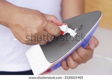 Close up hand squeeze toothpaste to clean stain on iron appliance surface. Concept, household tool treatment maintenance. Repair, electric equipment. Trick for solving problems burning stain.        