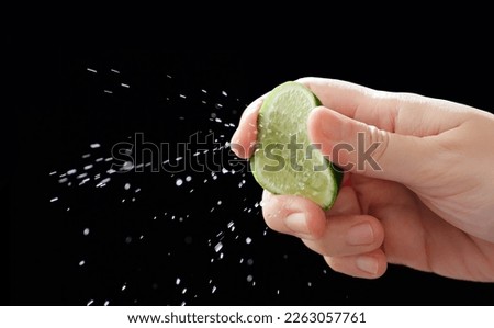 Close up of hand squeezing lemon, black background, splash of water