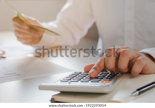 Close up hand of stress young asian\
businessman,male is pressing a calculator to calculate tax income\
and expenses, bills, credit card for payment or payday at home,\
office.Financial, finance\
concept.