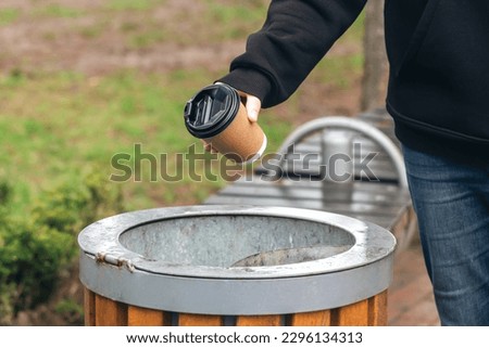 Close up hand throwing empty paper disposable coffee cup in recycling bin. Eco friendly approach concept.