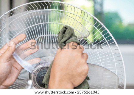 Close up hand touch rag dirty and dust on floor fan. unhealthy air flow. wipe, rub and wash, horizontal photo of hand cleaning dirty fan blade with cloth.
