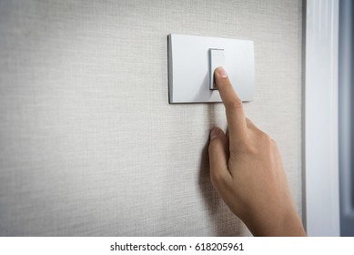 Close Up Hand Turning On Or Off On Grey Light Switch With Texture Background Of Interior Wall At The House Or Hotel. Copy Space.