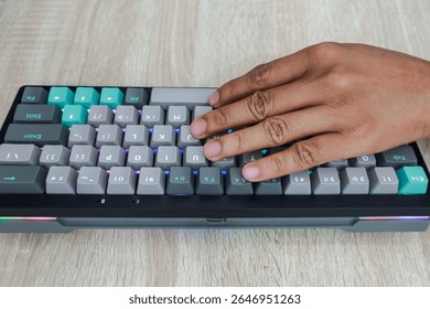 Close up of a hand typing on a small, customized keyboard with teal, gray, and beige keys on a