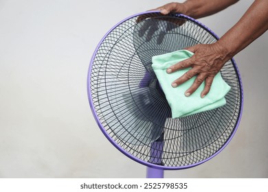 Close up hand use soft cloth to clean electric fan. Concept, Appliance maintenance and repair for long using. Clean dust on fan to stop allergy for hygiene. Chore and household keeping.               
