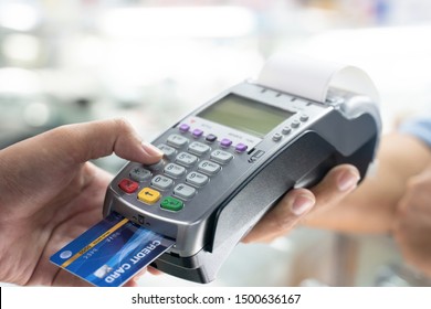 Close Up Of Hand Using Credit Card Swiping Machine To Pay. Hand With Creditcard Swipe Through Terminal For Payment In Cafeteria. Man Entering Credit Card Code In Swipe Machine.