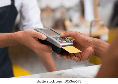 Close up of hand using credit card swiping machine to pay. Hand with creditcard swipe through terminal for payment in cafeteria. Man entering credit card code in swipe machine.