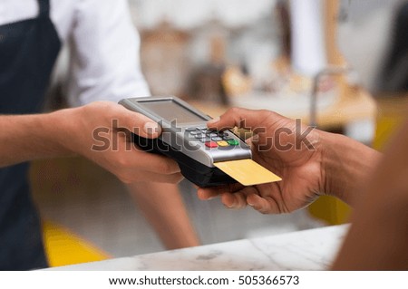 Close up of hand using credit card swiping machine to pay. Hand with creditcard swipe through terminal for payment in cafeteria. Man entering credit card code in swipe machine.