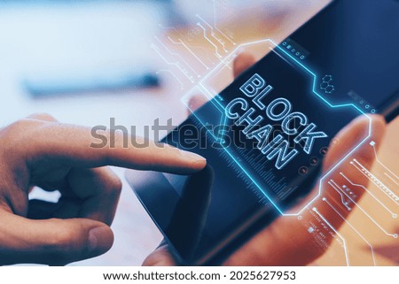 Close up of hand using digital tablet with creative blockchain hologram on blurry wooden office desktop background. Cryptocurrency and finance concept. Double exposure
