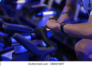 close up hand using smart watch while exercising on exercise bicycle in gym room at night. blur background