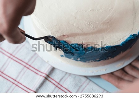 Close up of hand using spatula to apply blue frosting on homemade cake, smooth cream texture and decorating process.