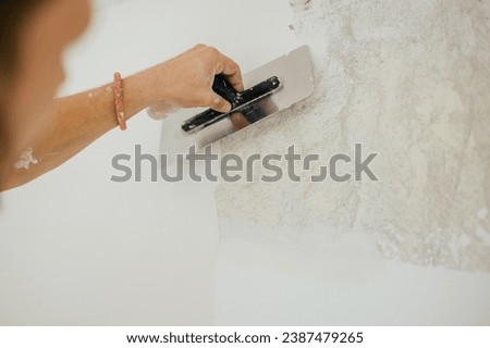 Close up of hand using trowel for plastering and skim coating wall. A builder's hand using trowel and plaster for plastering and skim coating wall. A plasterer is doing plasterwork. Copy space.