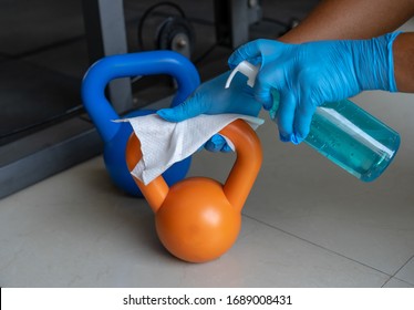 Close Up Of Hand Using Wet Wipe And Sanitizer Alcohol Spray Bottle To Clean Kettlebell In Gym.Antiseptic,disinfection,cleanliness And Healthcare,Anti Bacterial And Corona Virus (COVID-19).