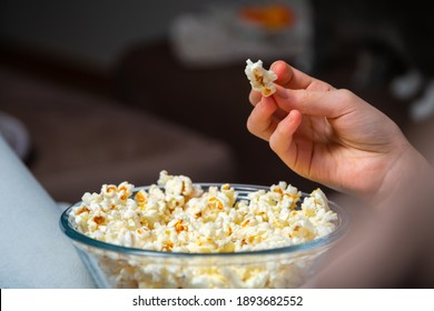 Close Up Of Hand Waking Popcorn From A Bowl While Watching TV. Person Sitting In Comfortable Couch And Watching Home Cinema In The Dark.