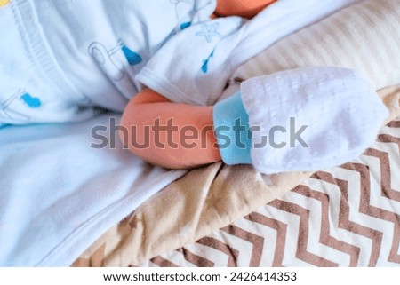 A close up of baby’s hand wearing mitten laying on a blanket