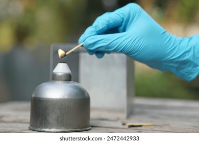 Close up hand wears blue glove, hold a burning match  to light fire on alcohol lantern or laboratory lamp. Concept, equipment or tool for science experiment.                                      - Powered by Shutterstock