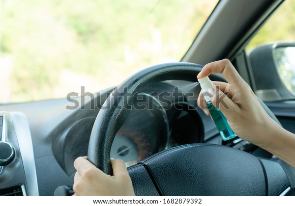 Close up hand of woman disinfecting car steering\
wheel by spraying alcohol from a bottle, protection against\
infectious virus, bacteria and germs. Coronavirus/ Covid-19, health\
care concept.