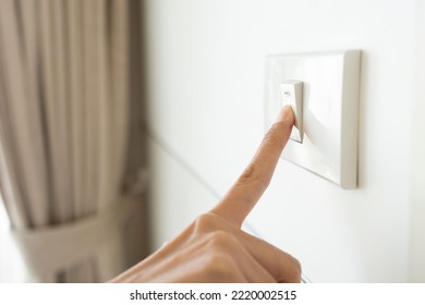 close up hand of woman turning off light switch in a home.