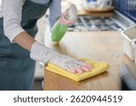Close up hand of woman wearing rubber gloves cleaning wooden kitchen counter using clothes and cleaning solution. Home cleaning cooking hygienic wood surface care concept.