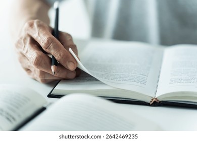Close up of hand writing notes in open book Textbook reading or note taking. Concept of literature studying, academic learning or exam preparation. Education knowledge at home or school or university