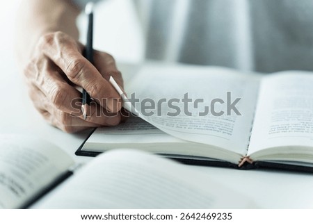 Close up of hand writing notes in open book Textbook reading or note taking. Concept of literature studying, academic learning or exam preparation. Education knowledge at home or school or university