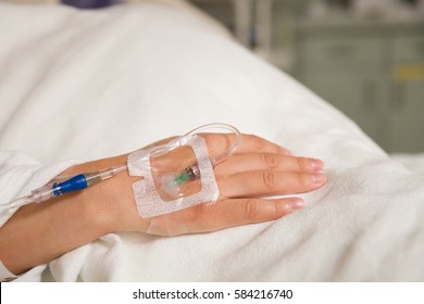 Close up hand of young patient with intravenous catheter for injection plug in hand during lying in the hospital bed. 