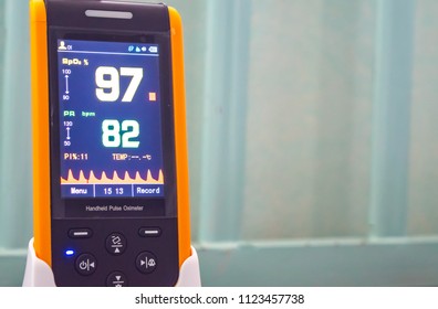 Close Up Handheld Pulse Oximeter, Medical Instrument Use To Monitor Blood Oxygen In Patient In Hospital, Showing Normal Blood Oxygen Ninety-seven In Yellow And Pulse Rate Eighty-two In Green. 