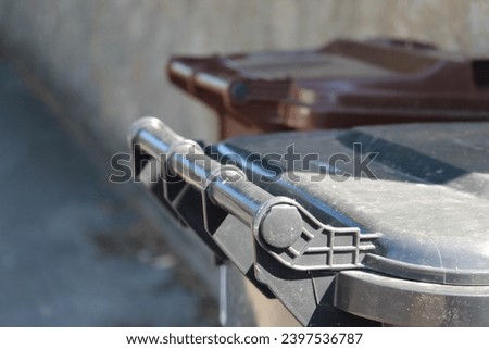 A close up of the handle on a black bin on a path. 