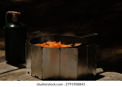 Close up of hands adding shredded carrots to a cast iron pot cooking on a portable camp stove outdoors