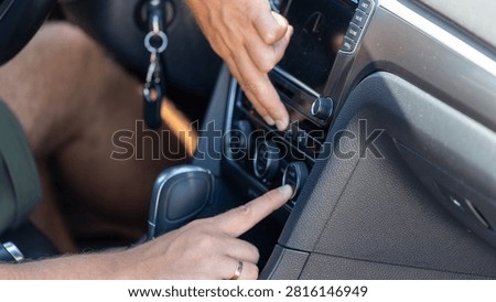 Close up of hands adjusting climate control and multimedia settings inside a modern car. Driver operating air conditioning and dashboard controls.