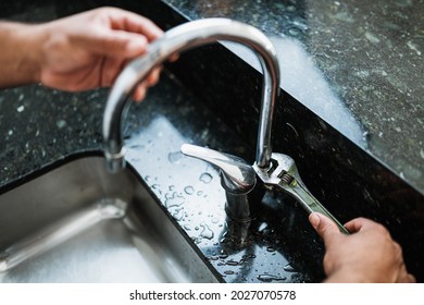 Close up of hands of aged repairman fixing broken kitchen tap using adjustable wrench. Repair service concept. - Shutterstock ID 2027070578