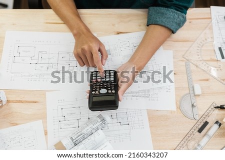 Close up hands of Architect or Engineer pressing on calculator for calculating value estimating for safety with the drawing construction building.