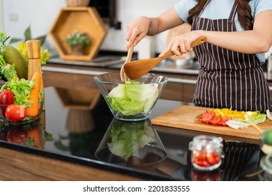 Close up hands of Asian woman wearing apron, tossing the vegetarian salad with wooden spatulas. Preparing a healthy salad with fresh vegetables such as carrot, tomato cabbage and green oak. - Shutterstock ID 2201833555