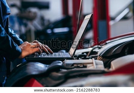 Close up hands of auto electrician using a computer laptop to diagnosing and checking up on car engines parts for fixing and repair