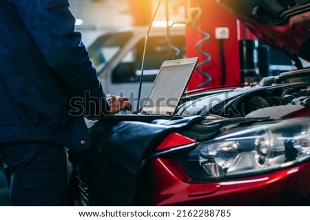 Close up hands of auto electrician using a computer laptop to diagnosing and checking up on car engines parts for fixing and repair