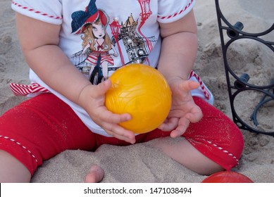 Close Up Of Hands Of A Baby Holding Yellow Bocce Ball On A Sand Beach