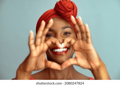Close up of hands of beautiful african woman making heart shape isolated against blue wall. Portrait of smiling middle aged black woman making heart gesture with hands around her big white smile. - Shutterstock ID 2080247824