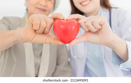 close up hands and blur people, asian female doctor and old patient holding red heart with hands, happiness and relationship in hospital, they feeling happy and smile on white background