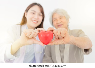 Close Up Hands And Blur People, Asian Female Doctor And Old Patient Holding Red Heart With Hands, Happiness And Relationship In Hospital, They Feeling Happy And Smile On White Background