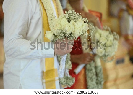 Close up of hands of bride and groom holding together at a traditional Indian wedding, groom holding flower. Selective focus.